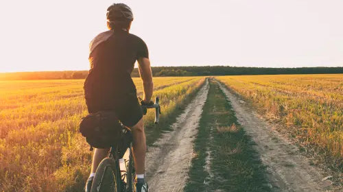 Man biking through a field on a gravel road.