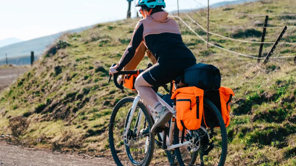 woman biking along a gravel road with bikepacking bags