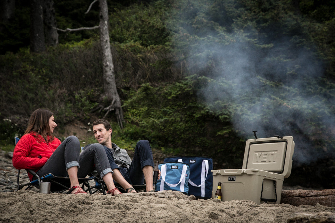 Couple sitting on a beach with cooler, drinks and tote bags.- North St. Bags all-groups