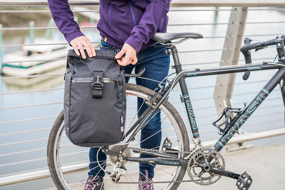 Cyclist on bridge closing the roll-top of a black pannier. - North St. Bags all-groups