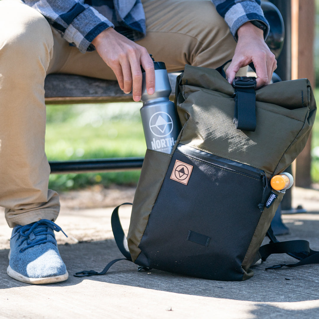 Guy sitting on park bench putting a water bottle into the side pocket of a Davis Daypack - North St. Bags all-groups