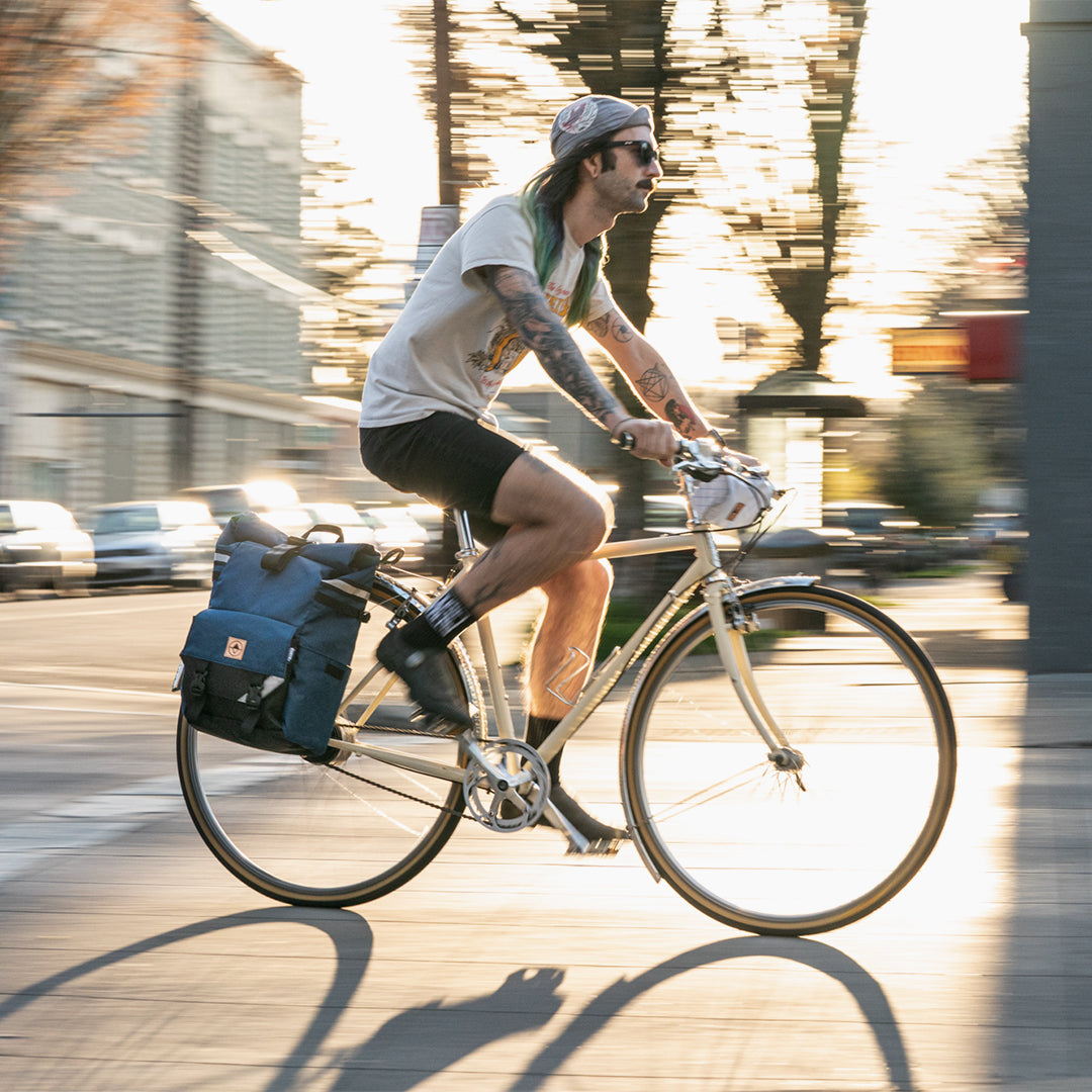 Guy riding bike on a city street with a Woodward bag as a pannier. - North St. Bags all-groups