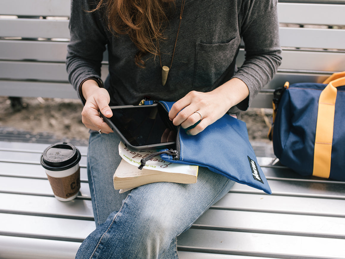 Woman stowing a tablet inside a large pouch on a park bench.  - North St. Bags all-groups