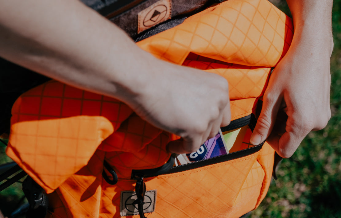 hands reaching into front pocket of a blaze orange Bikepacking 澳洲5结果记录 pannier