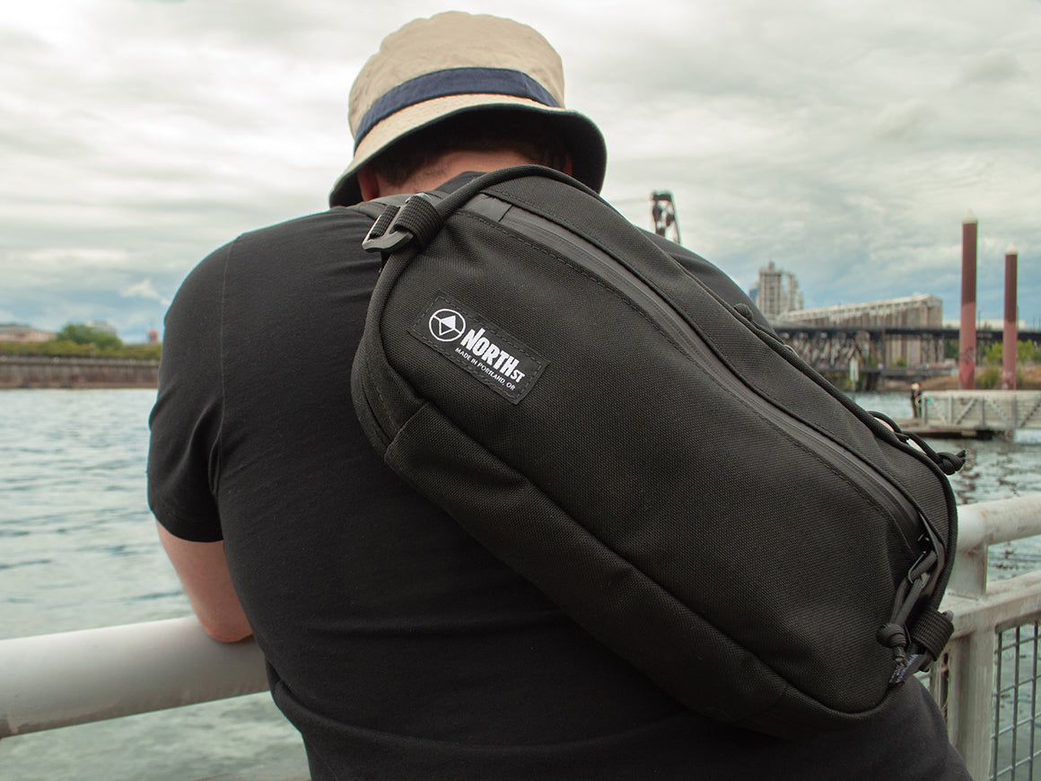 man at waterfront wearing a black sling pack all-groups