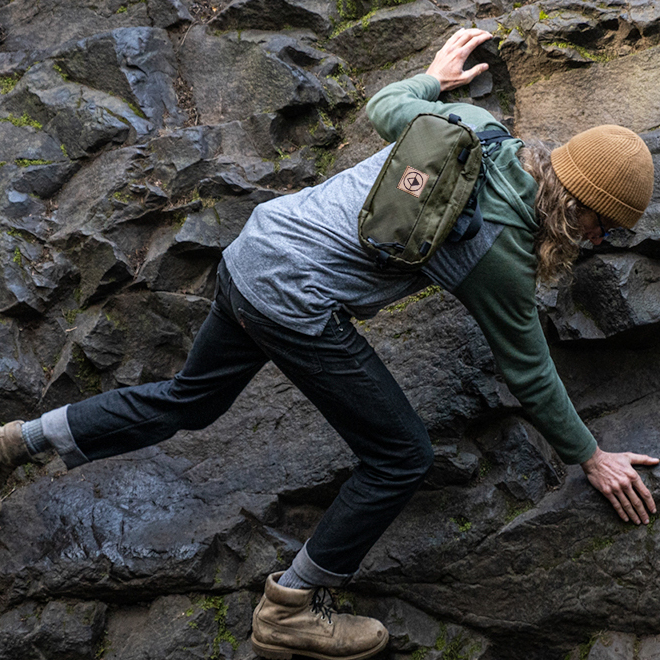 hiker with green sling pack climbing on a rock face