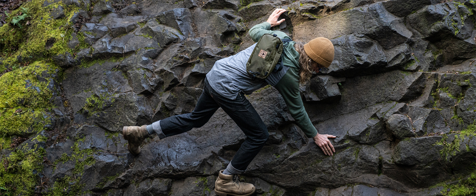 hiker with green sling pack climbing on a rock face