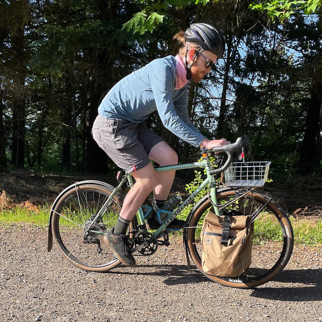 Male cyclist riding on a gravel path with coyote pannier. Macro Pannier - North St. Bags all-groups