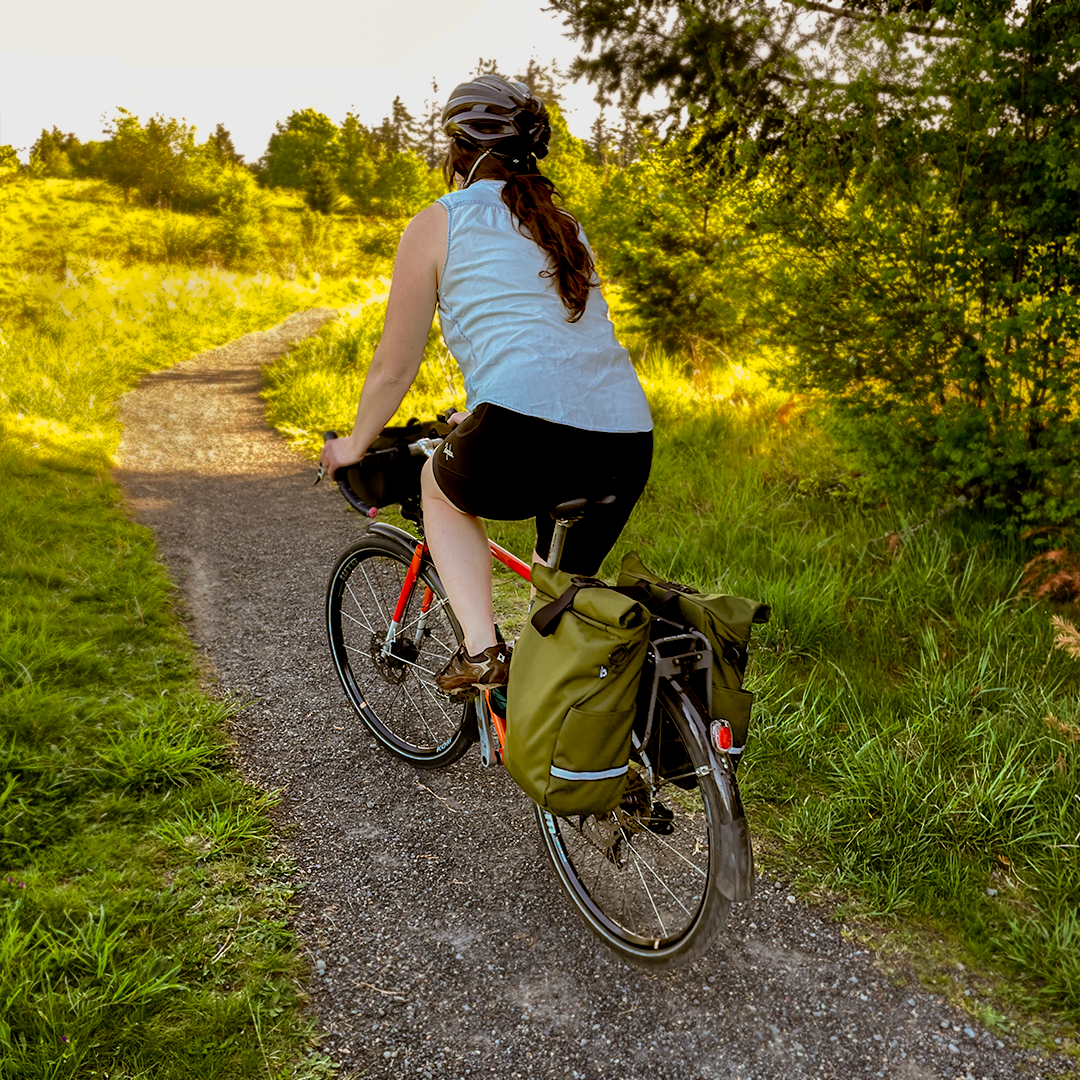 Woman cyclist riding along a gravel trail with panniers - North St. Bags all-groups