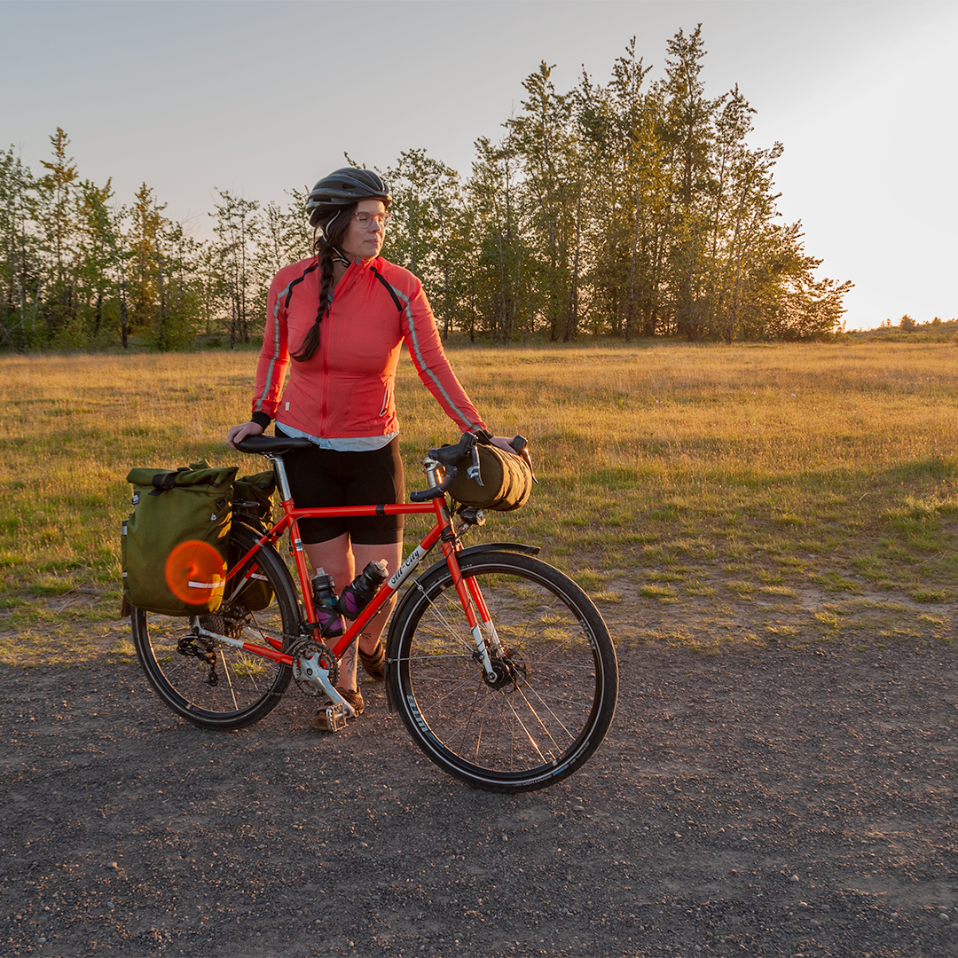 Woman cyclist walking her bike along a gravel path with panniers and a handlebar bag. - North St. Bags all-groups